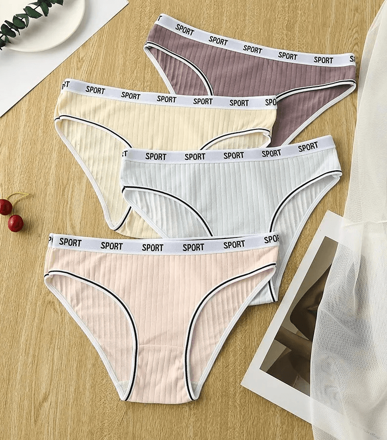 Four pairs of women's low-rise cotton panties in solid colors on a wooden surface, featuring a 'SPORT' waistband design.